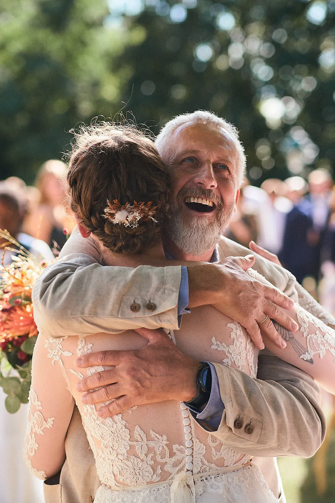 Ein Vater umarmt seine Tochter im Brautkleid sehr emotional und stahlt vor Freude und Stolz.