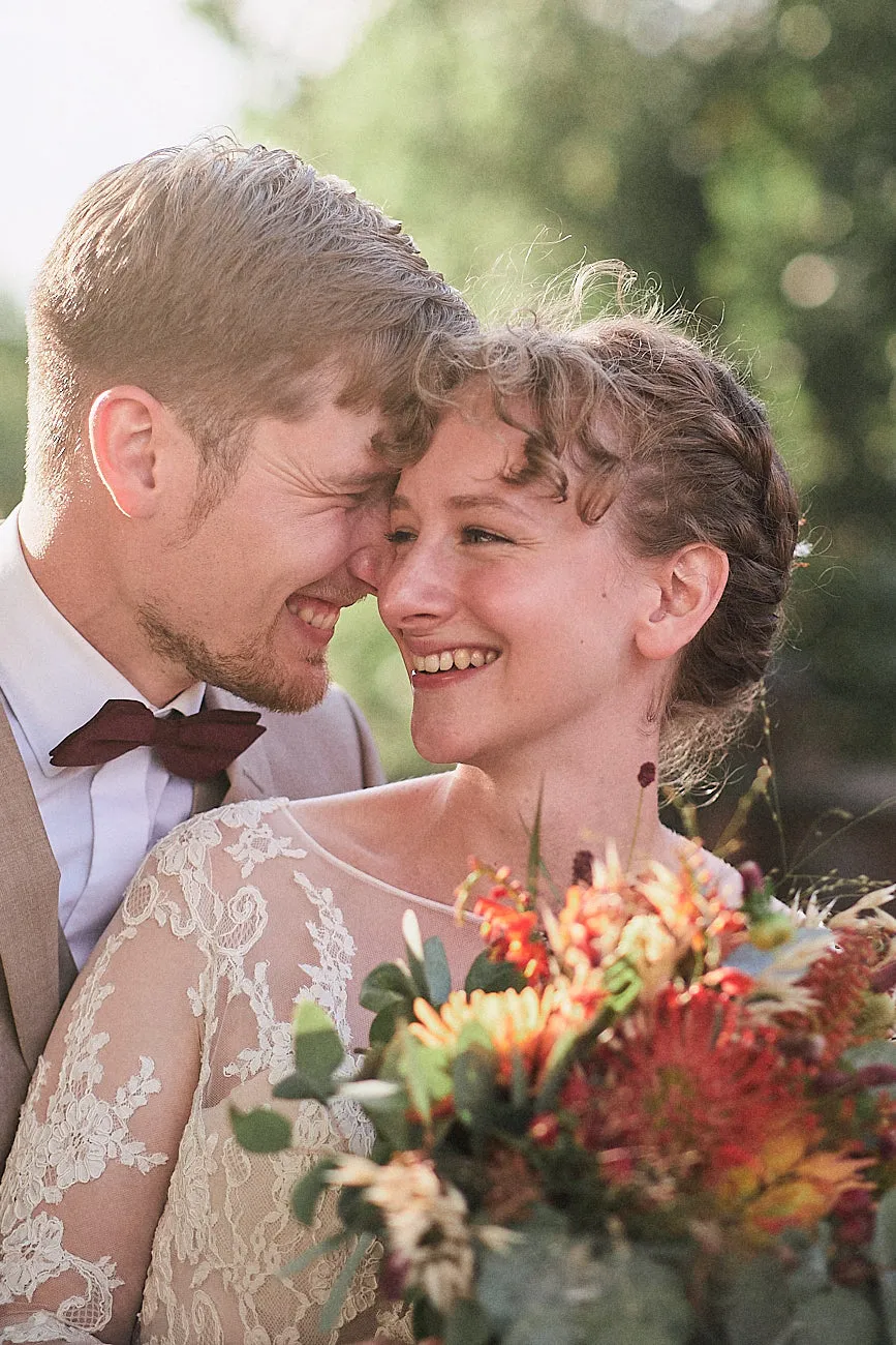 Hochzeitspaar steht im Grünen und hält die Stirn aneinander. Beide lächeln als ob jemand gerade einen Wirtz gemacht hat.
