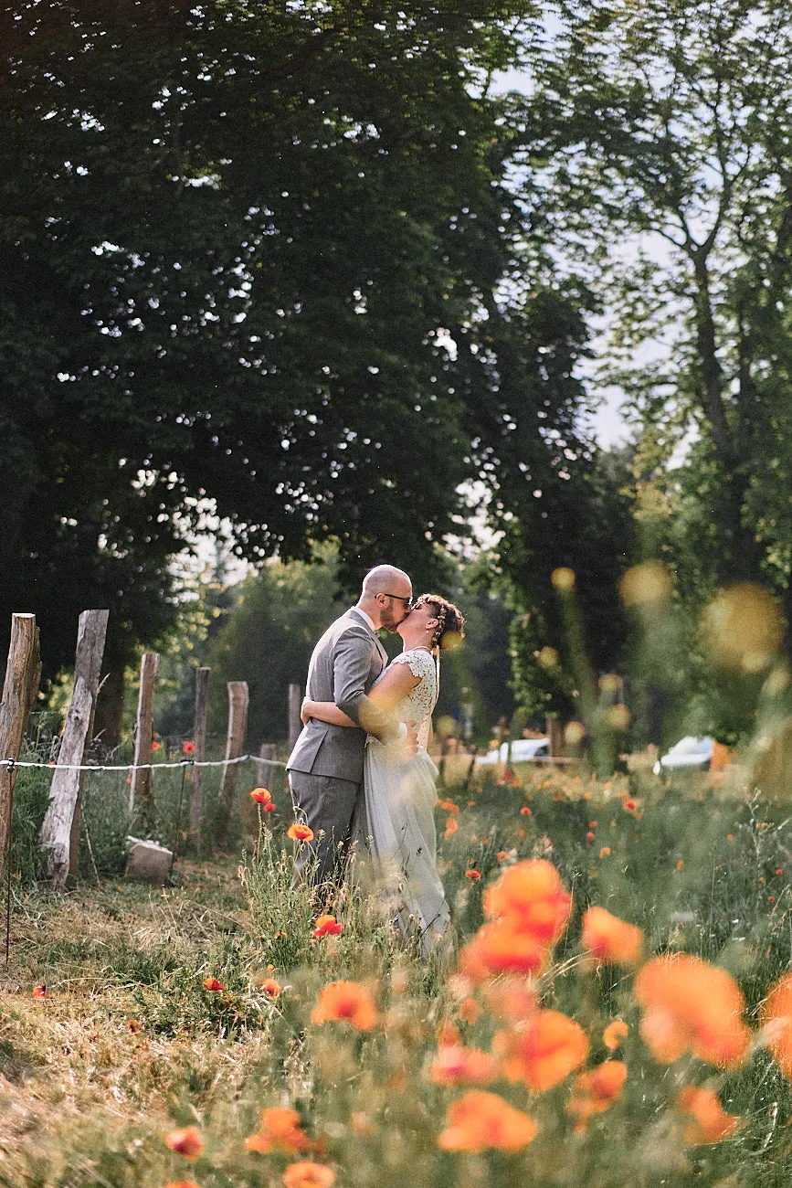 Ein Hochzeitspaar küsst sich auf deiner Wiese voller Mohnblumen.